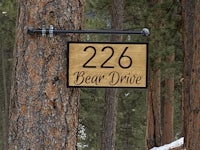 a wooden bear drive sign hangs on a tree in the woods
