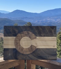 the colorado flag is on a wooden board with mountains in the background